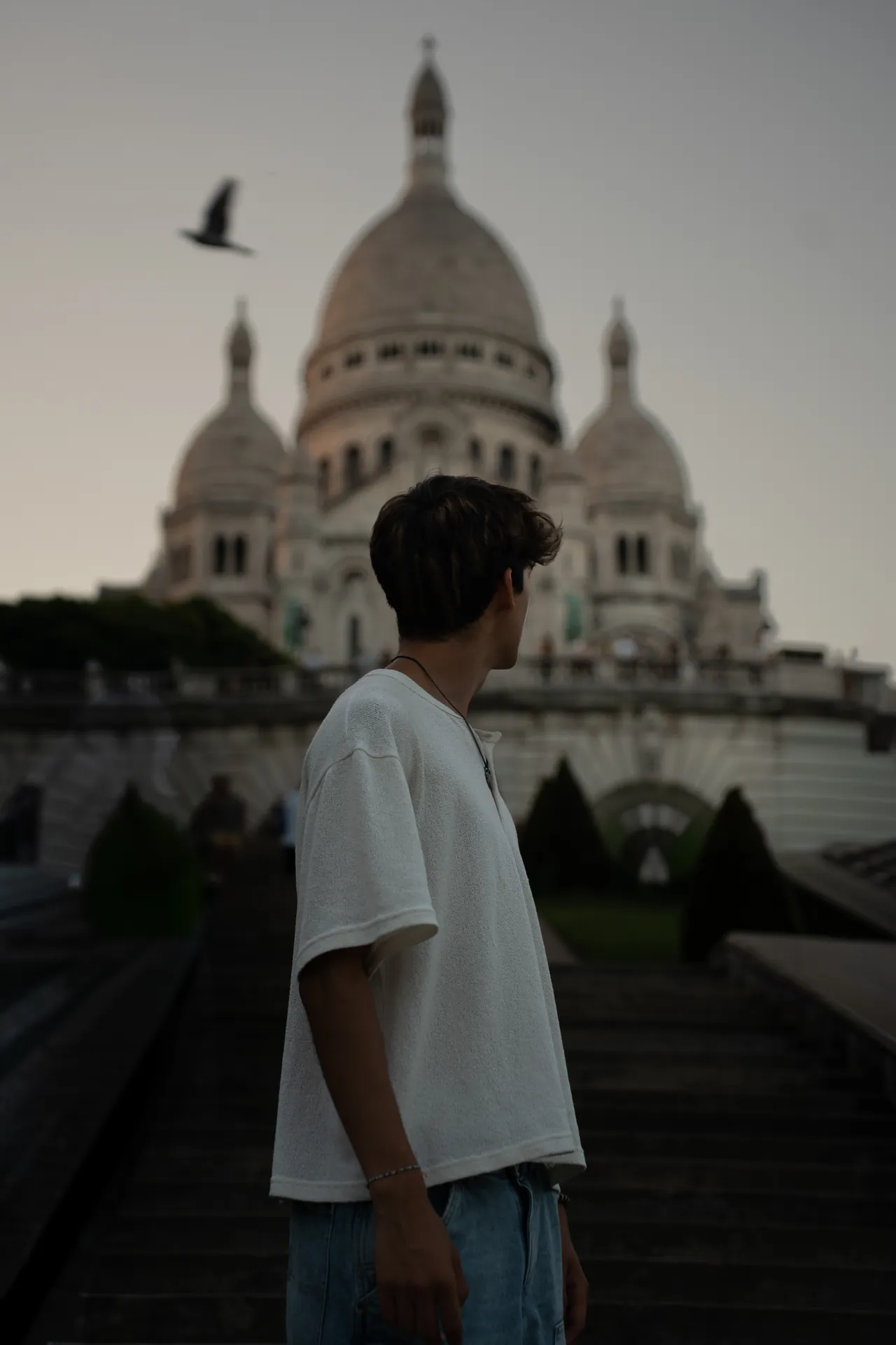 Lucas de espaldas, con camiseta blanca, frente al Sacré-Cœur de París mientras pasa un pájaro