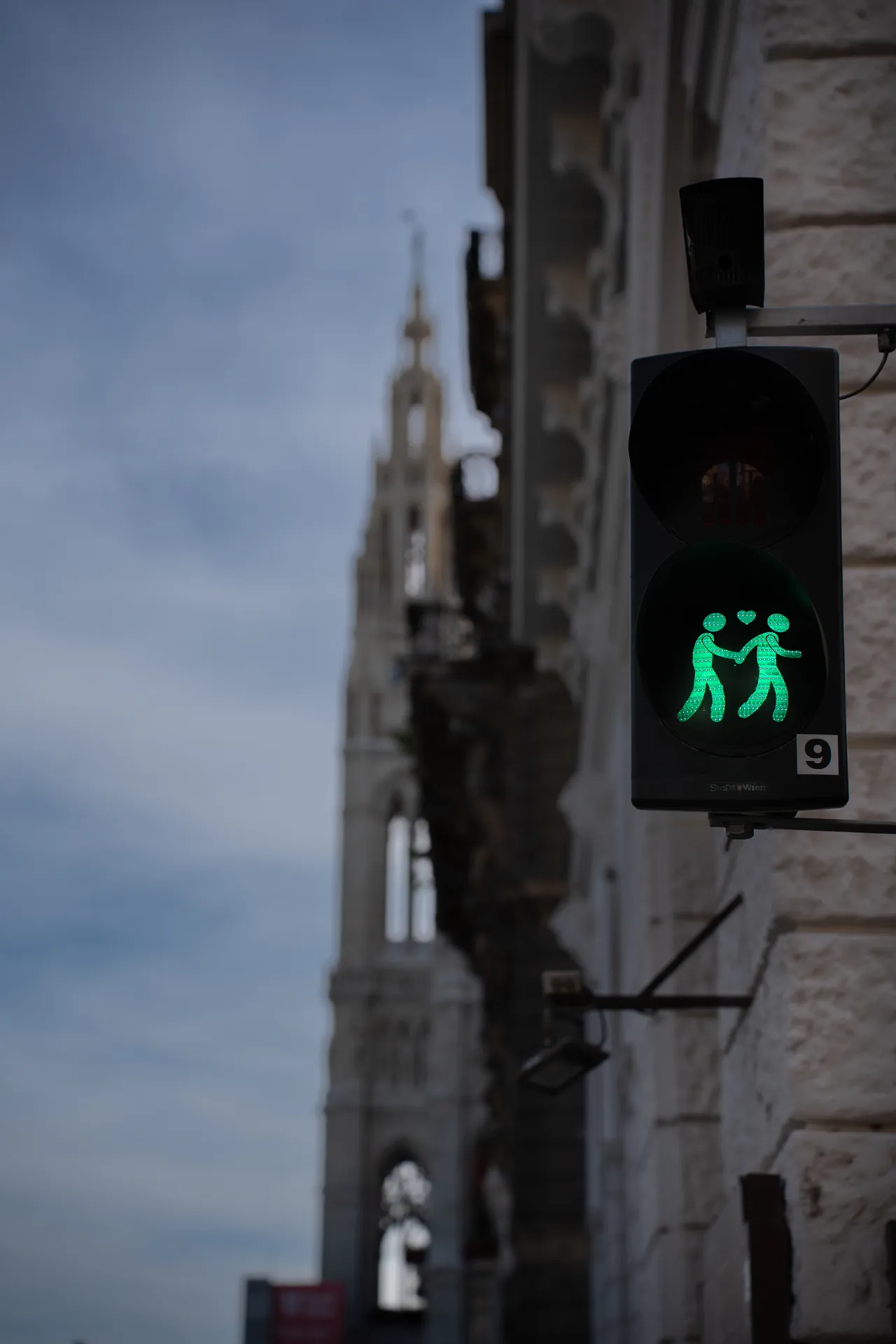 Semáforo peatonal con una pareja en verde frente a una torre gótica desenfocada