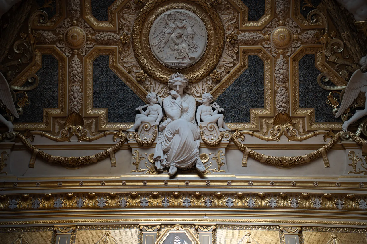 Techo dorado con una escultura de mujer sentada entre querubines