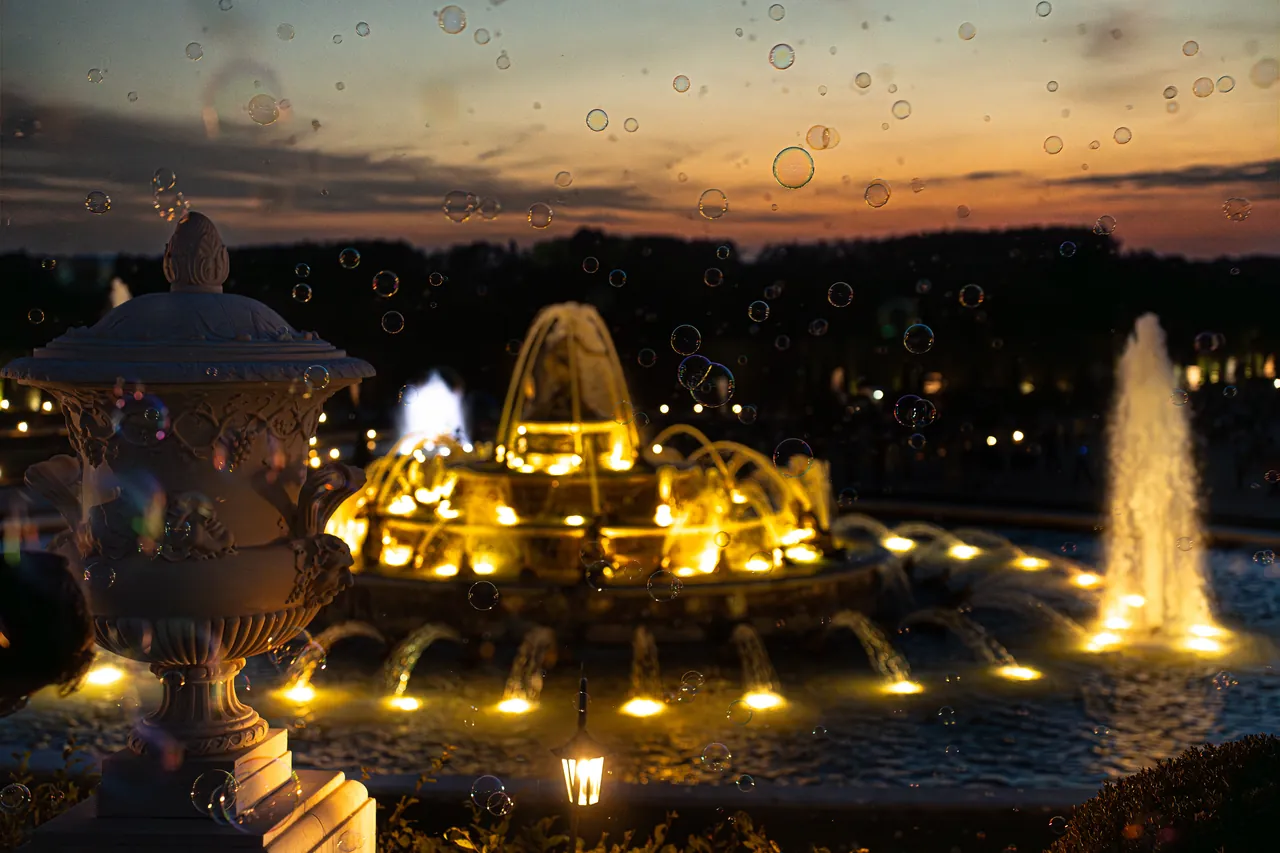 Fuente iluminada al anochecer con pompas de jabón flotando en el aire