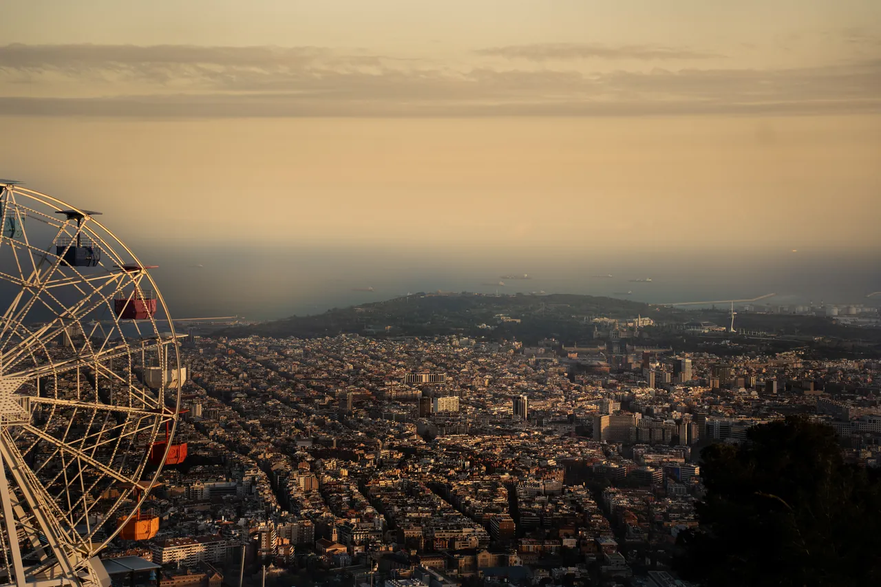 Noria sobre una ciudad extensa envuelta en la bruma del atardecer