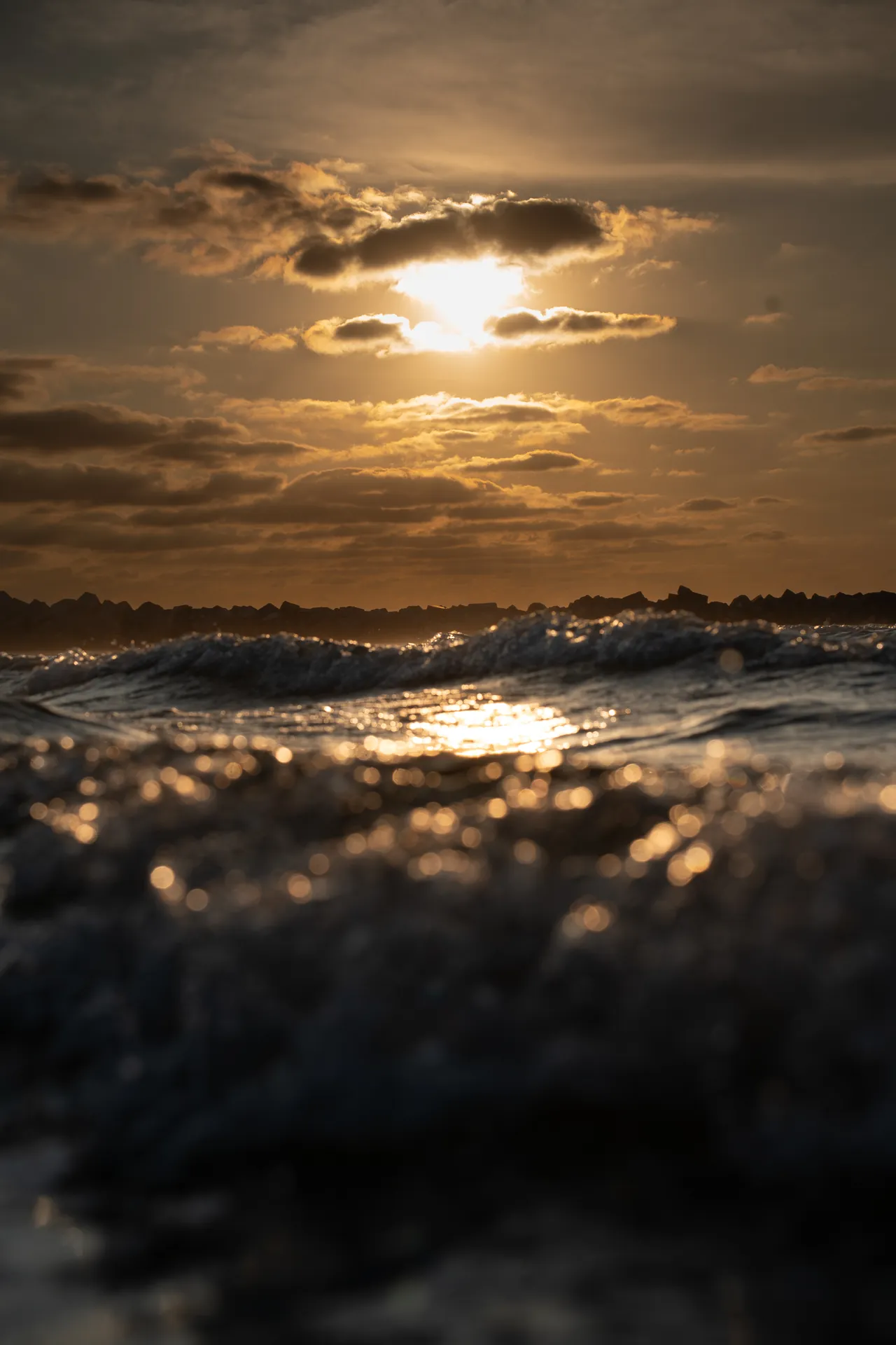 El sol atravesando las nubes sobre el mar, con olas en primer plano