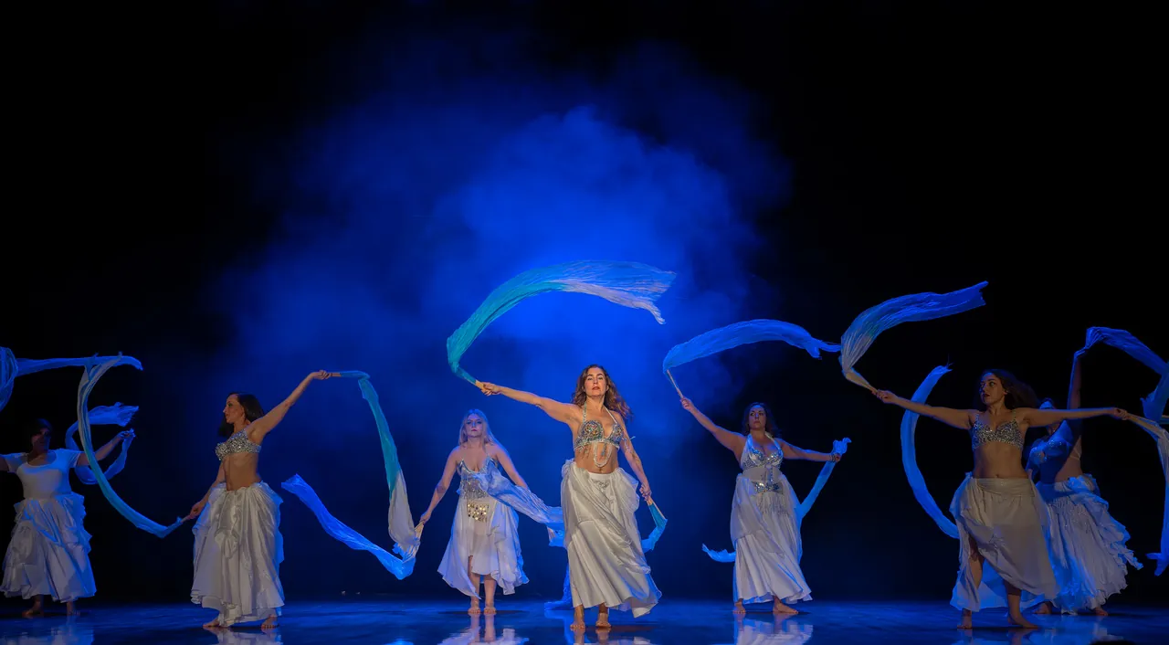 Bailarinas con velos azules ondeando sobre un escenario lleno de humo azul