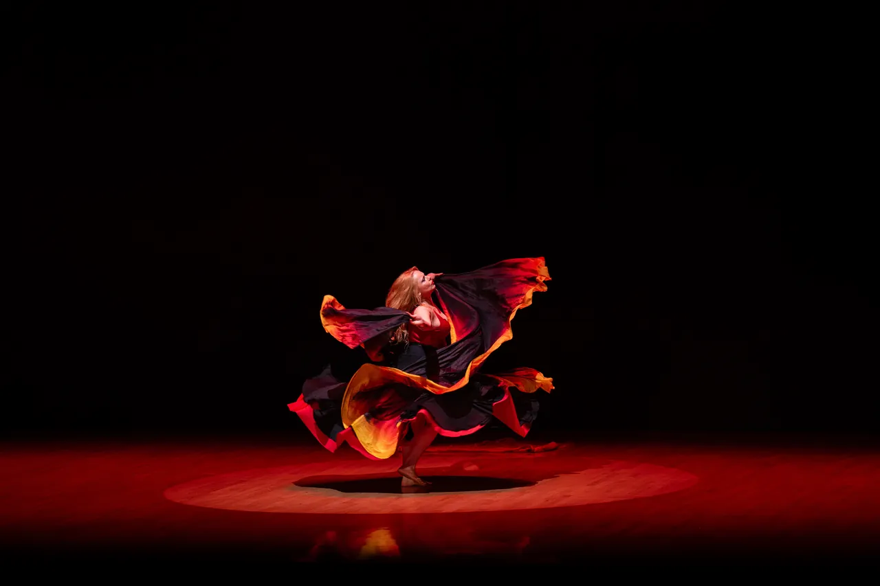 Bailarina girando una falda roja y naranja dentro de un foco rojo