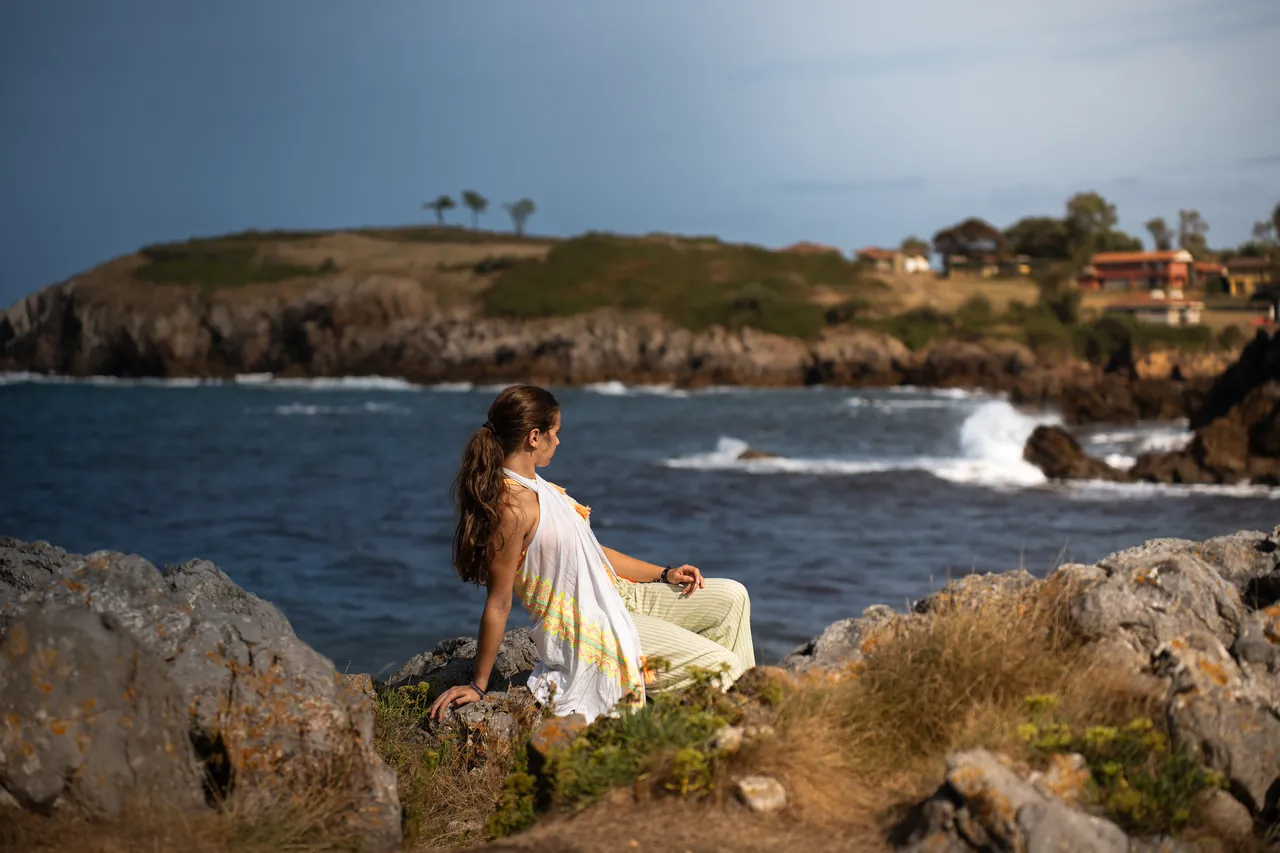Mujer con vestido blanco sentada en las rocas frente al mar