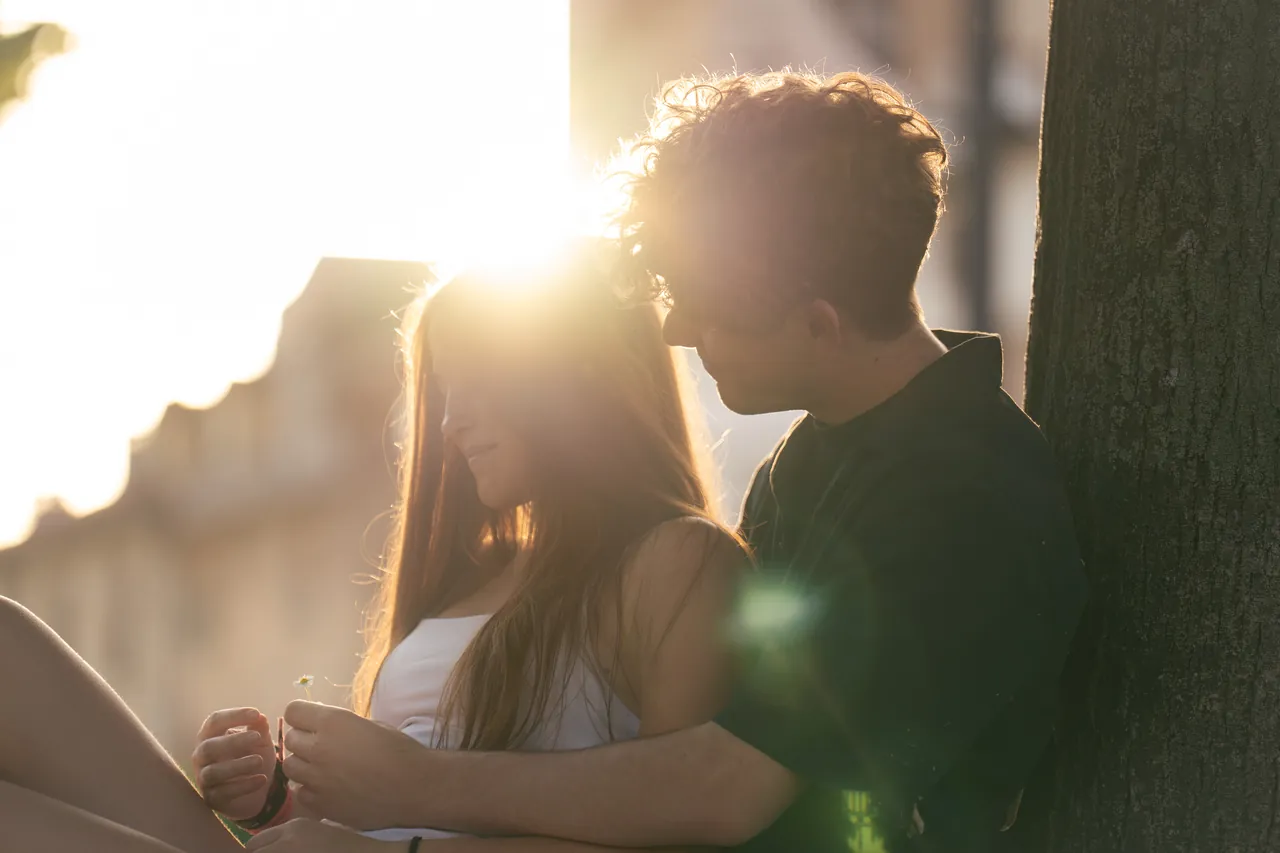 Pareja sentada bajo un árbol con un destello de sol