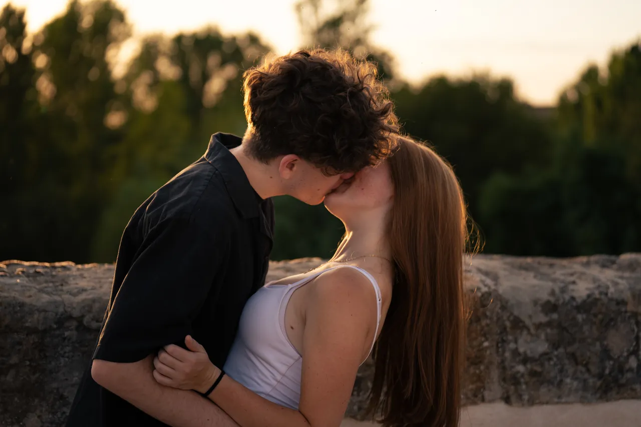 Pareja besándose al atardecer junto a un muro de piedra