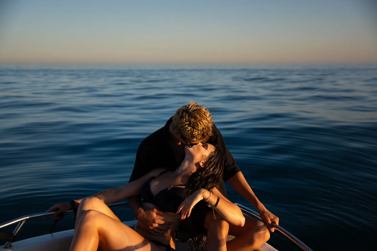 Pareja abrazada en una barca en mar abierto al anochecer