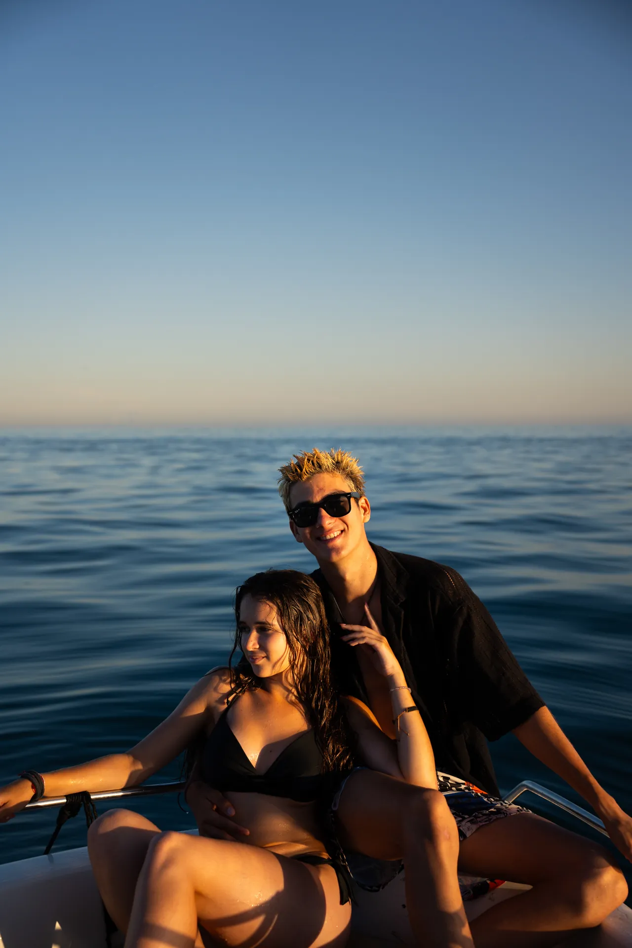 Pareja en una barca en mar abierto, él con gafas de sol