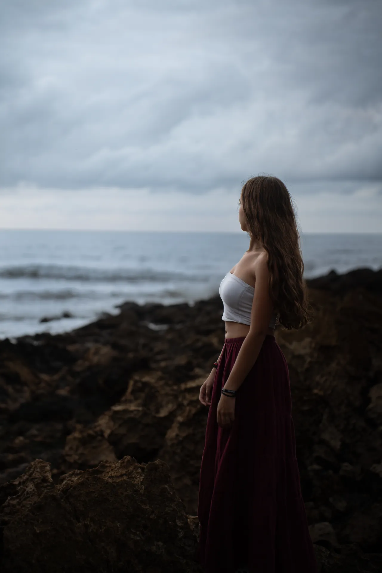 Chica en la costa rocosa mirando al mar bajo un cielo nublado